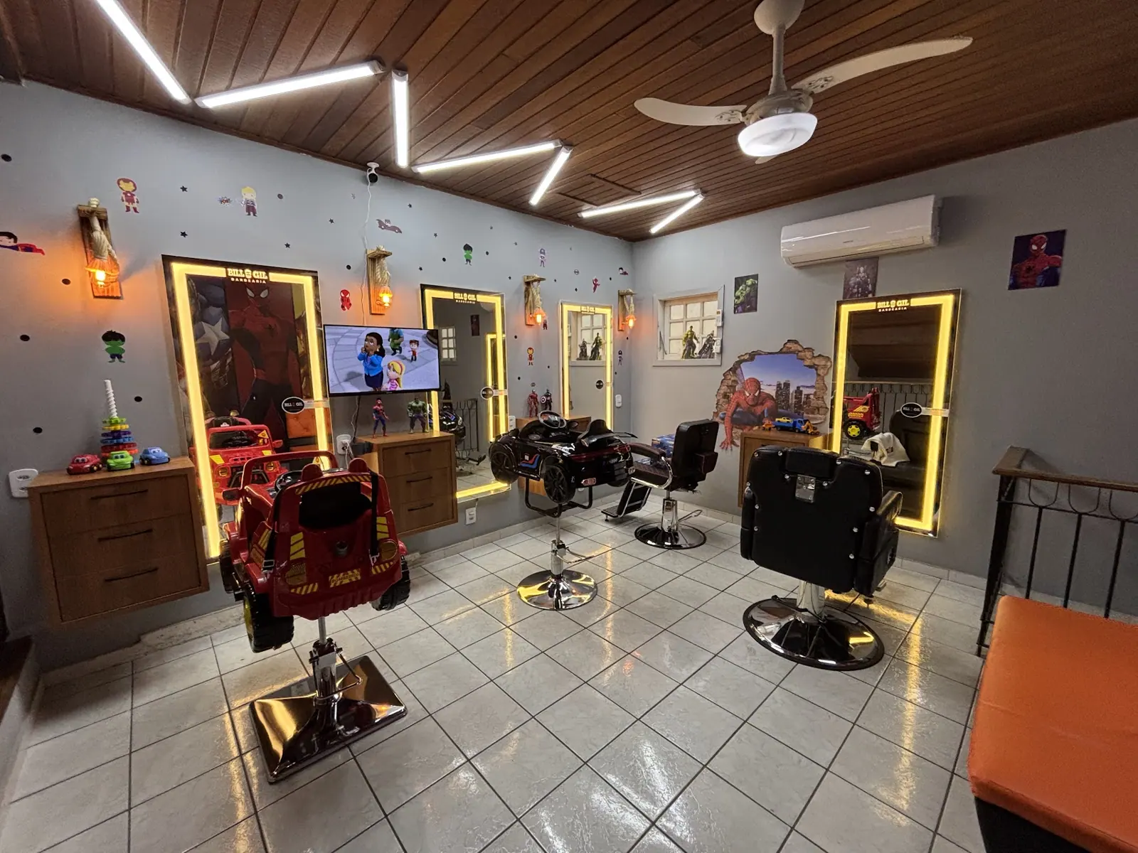 Salão da Bill & Gil com cadeira em forma de jipe vermelho, espelhos com luz de LED e cadeiras de barbeiro