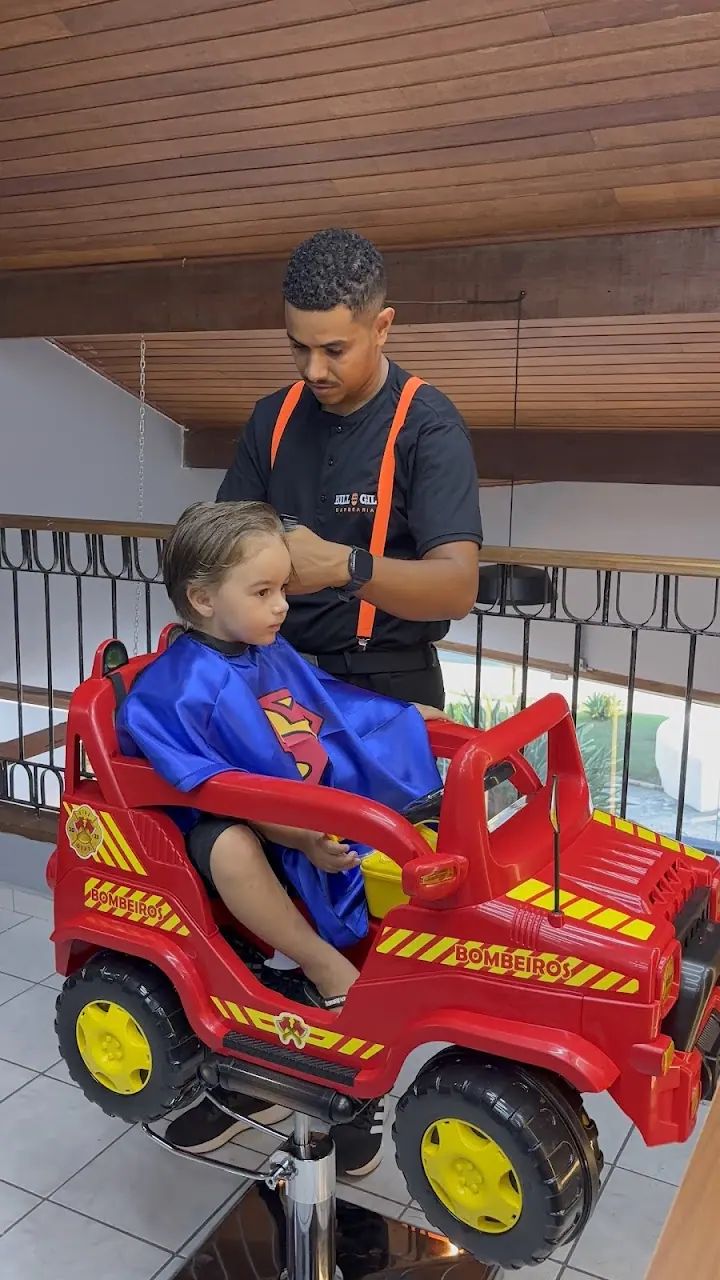 Menino sentado num jipe vermelho de brinquedo enquanto o barbeiro corta seu cabelo