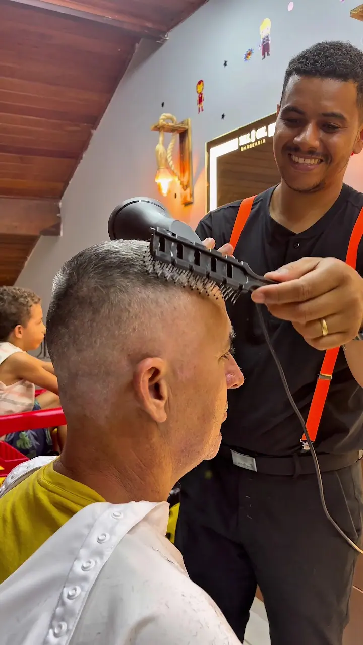 Barbeiro de suspensório laranja finalizando o corte com secador